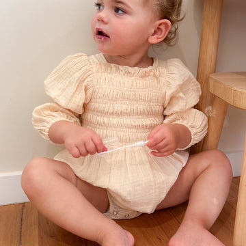 Baby wearing white cotton gauze romper with smocked bodice and puff sleeves