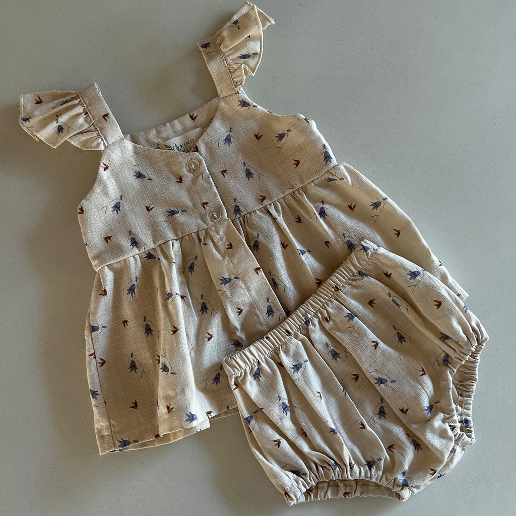 Neutral baby girls outfit with delicate bluebell and brown leaf design on latte cream cotton linen fabric